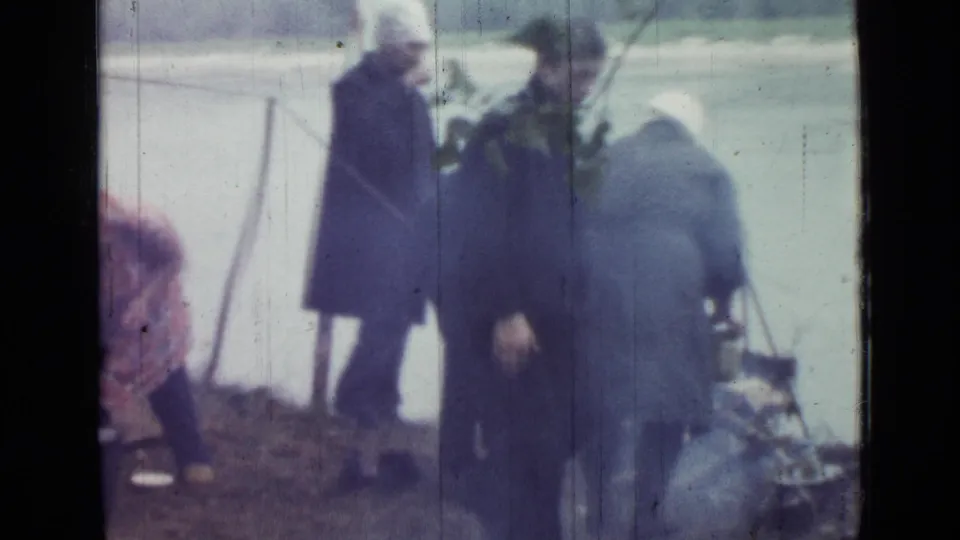 Two adults are prominent beside a lakeside tent in 1967 Russia home-movie footage, with camp gear and water behind them.