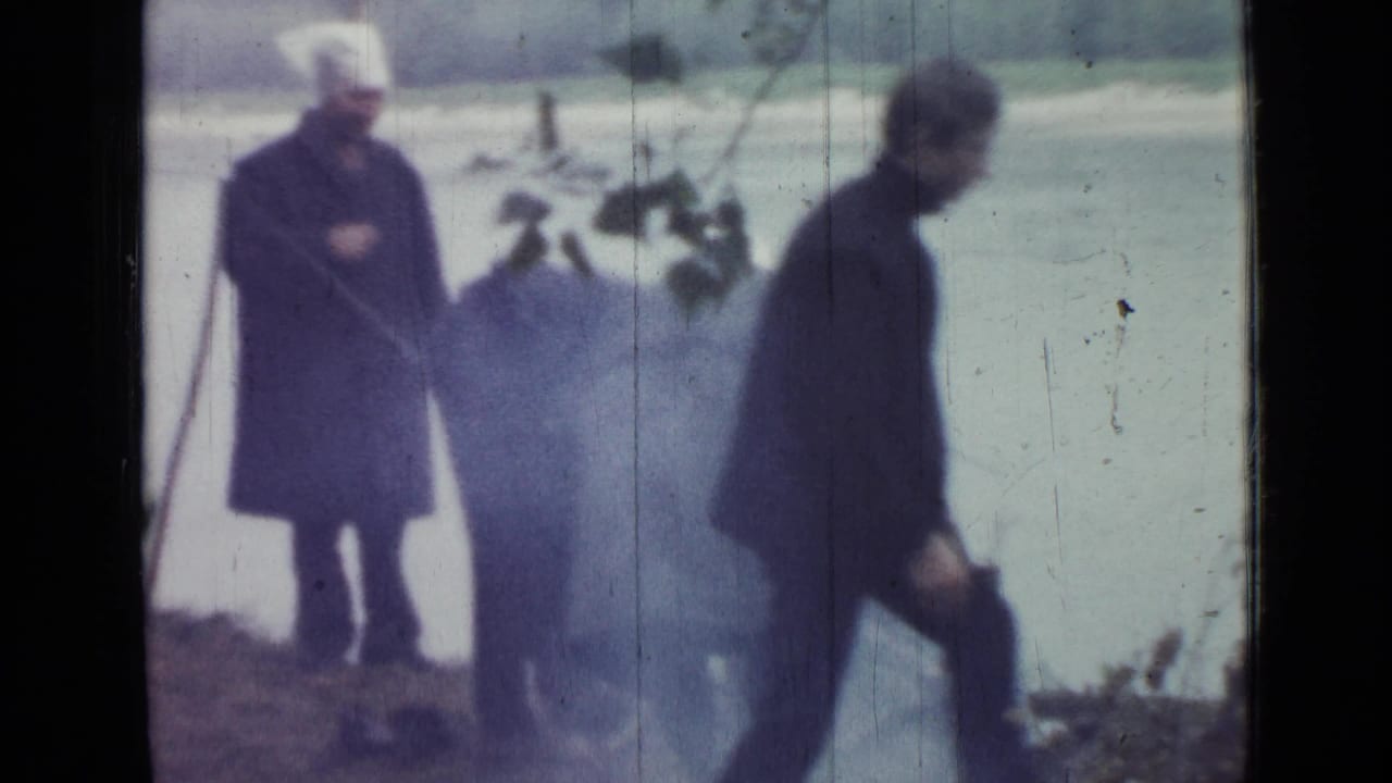 1967 lakeside camping frame showing one adult walking by the tent and another standing near a smoky cooking area.