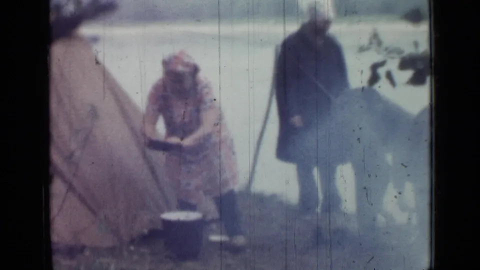 1967 Saint Petersburg home-movie frame showing a woman tending a pot near a tent while another adult stands nearby.