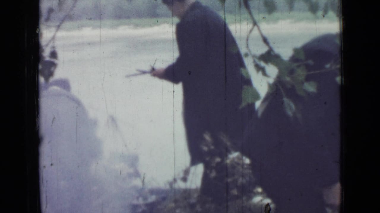 Soft 1967 home-movie frame showing a silhouetted adult near branches at a riverside campsite in Saint Petersburg.
