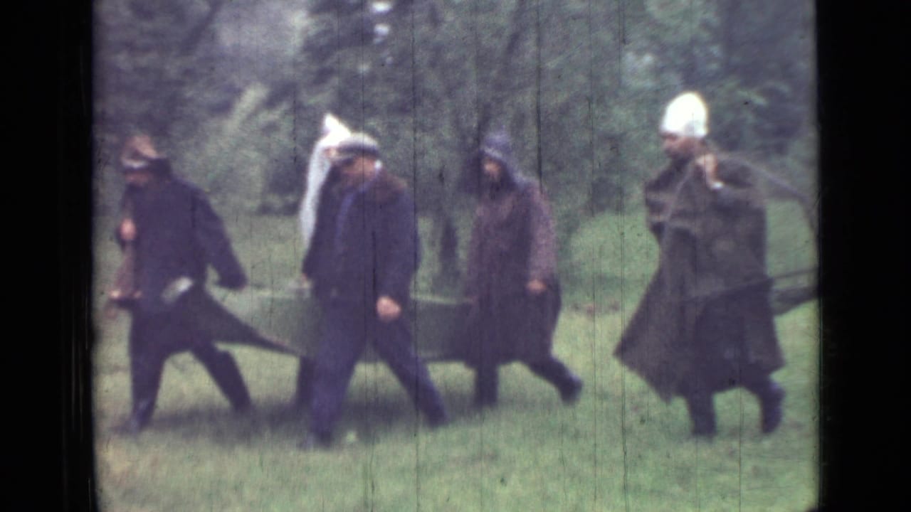 Men in dark coats walk across grass carrying green canvas sheets.