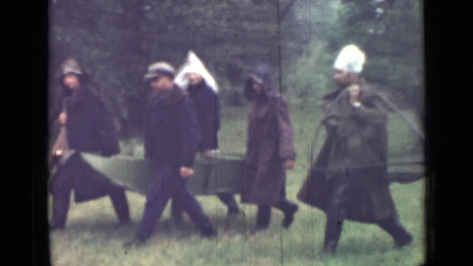 Adult men in plain dark garments proceed across grass in Saint Petersburg, with a white head covering and green canvas visible.