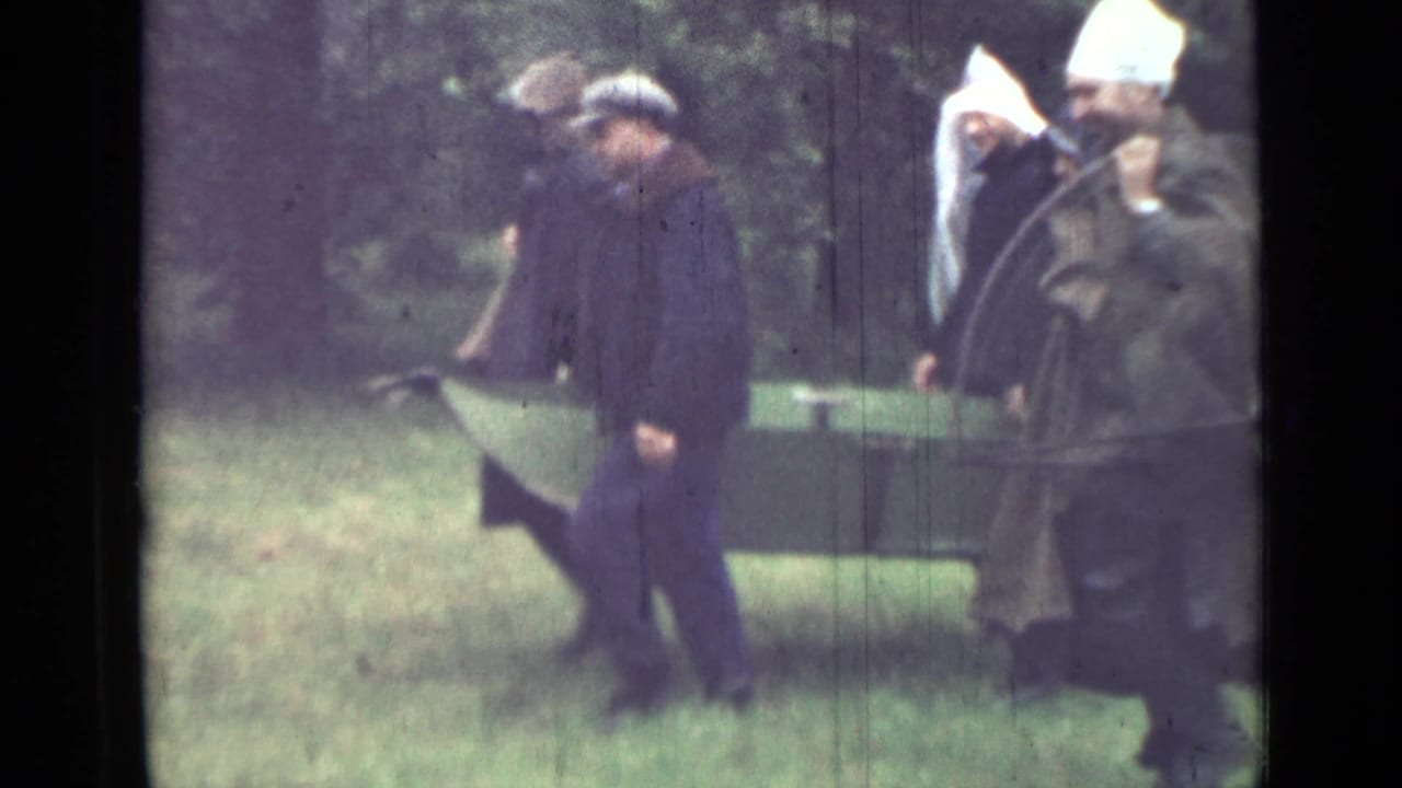 Near the end of the clip, men in plain dark clothing move beside a green canvas-covered object in the wooded Saint Petersburg setting.