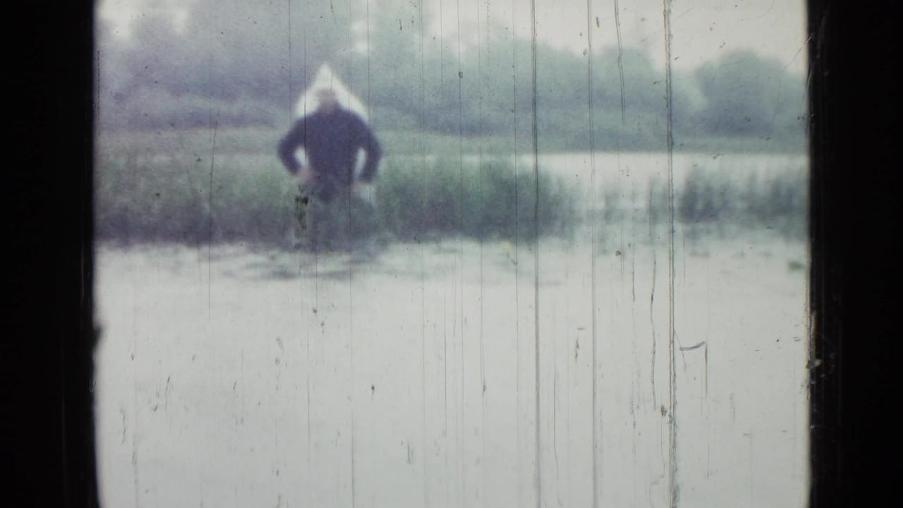 Distant person standing by a small lake, seen through a dark window frame.