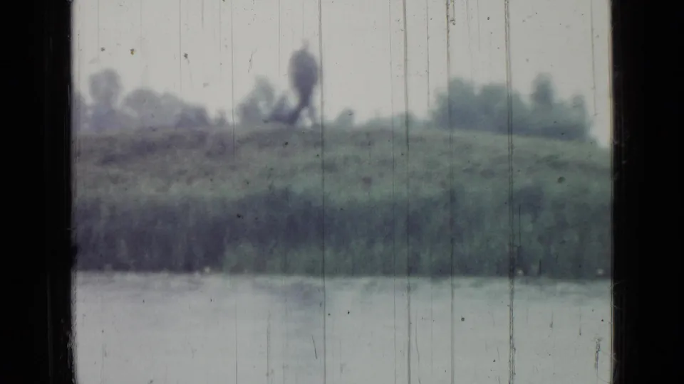 1967 Saint Petersburg home-movie view of a pond and grassy bank, with a blurred distant figure seen through rain-streaked vehicle glass.