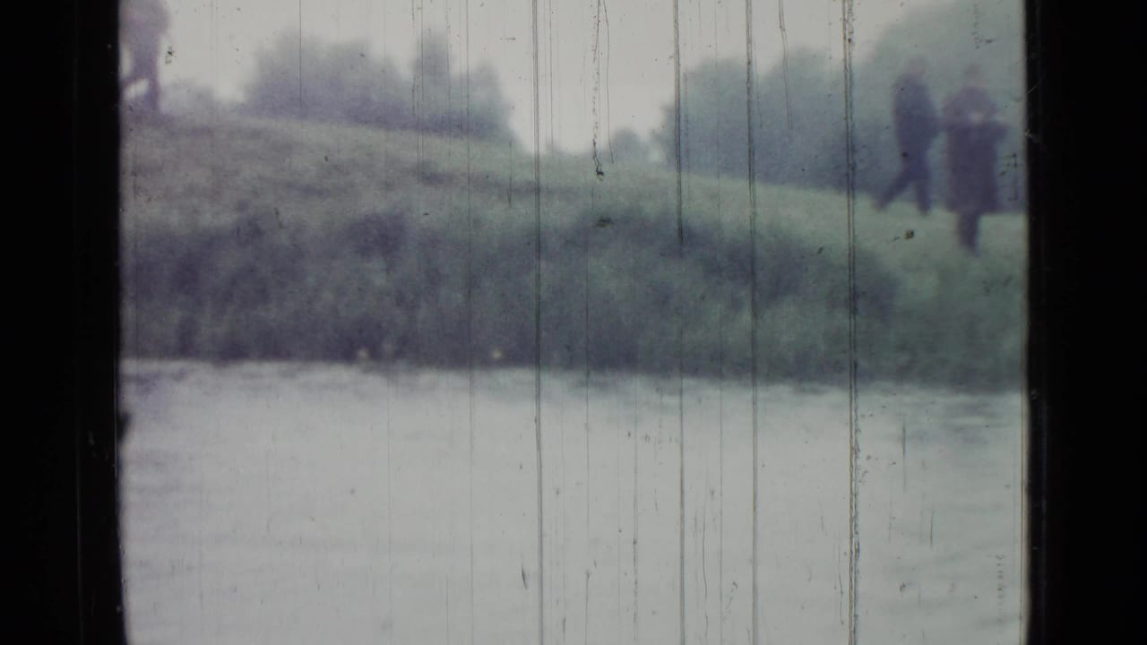 Blurred 1967 Saint Petersburg pond view with two dark-coated figures on the far bank, partly obscured by window framing and film scratches.