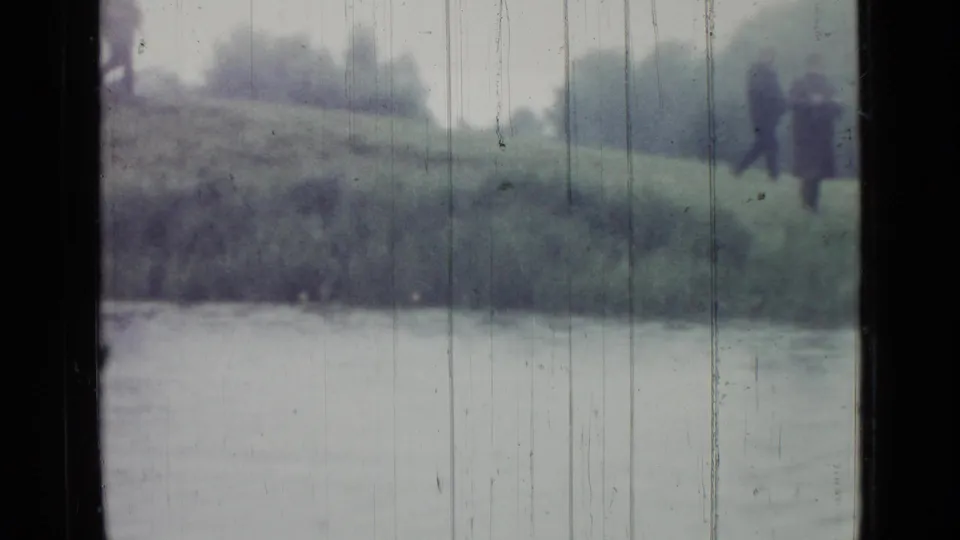 Blurred 1967 Saint Petersburg pond view with two dark-coated figures on the far bank, partly obscured by window framing and film scratches.
