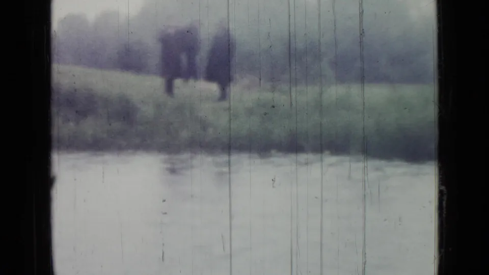 Soft 1967 Saint Petersburg waterside frame showing a dark-coated figure near a pond, distorted by motion, focus, and rain-marked glass.