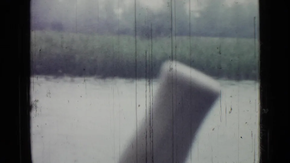 1967 Saint Petersburg pond view through rain-streaked glass, with the far bank and a pale blurred foreground shape inside or near the vehicle.