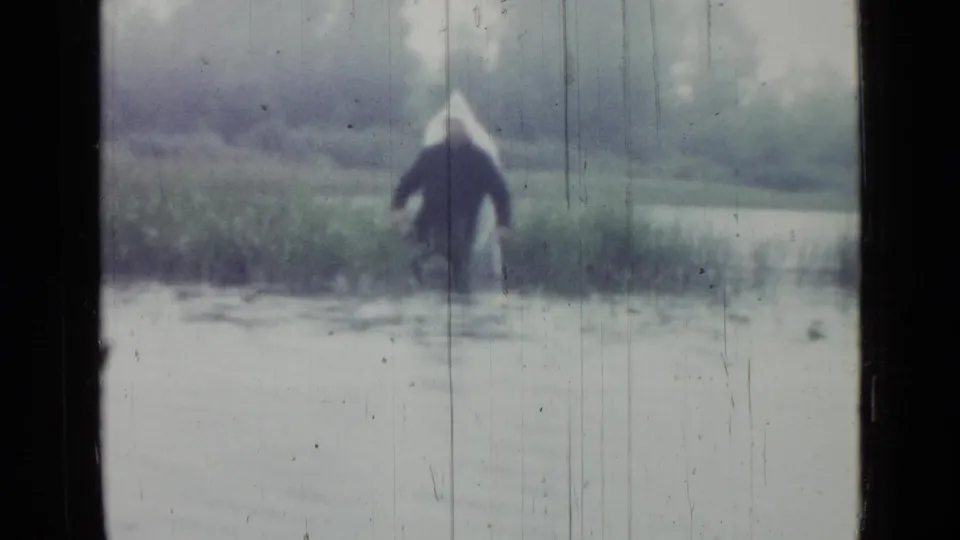 A distant figure in a light hat and dark coat wades through marsh water in the 1967 Saint Petersburg home movie.
