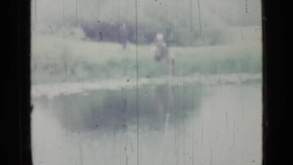 A soft, distant frame shows the figure near a reed-lined marsh, with reflective water and weathered 8mm texture.