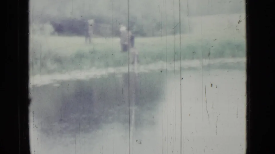 1967 Saint Petersburg 8mm frame showing a hazy small lake with grass and trees beyond the water.