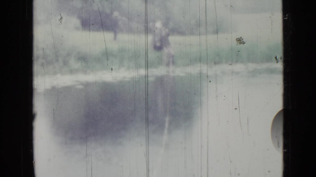 Distant figure near the shoreline beside a small lake, partly obscured by film wear.