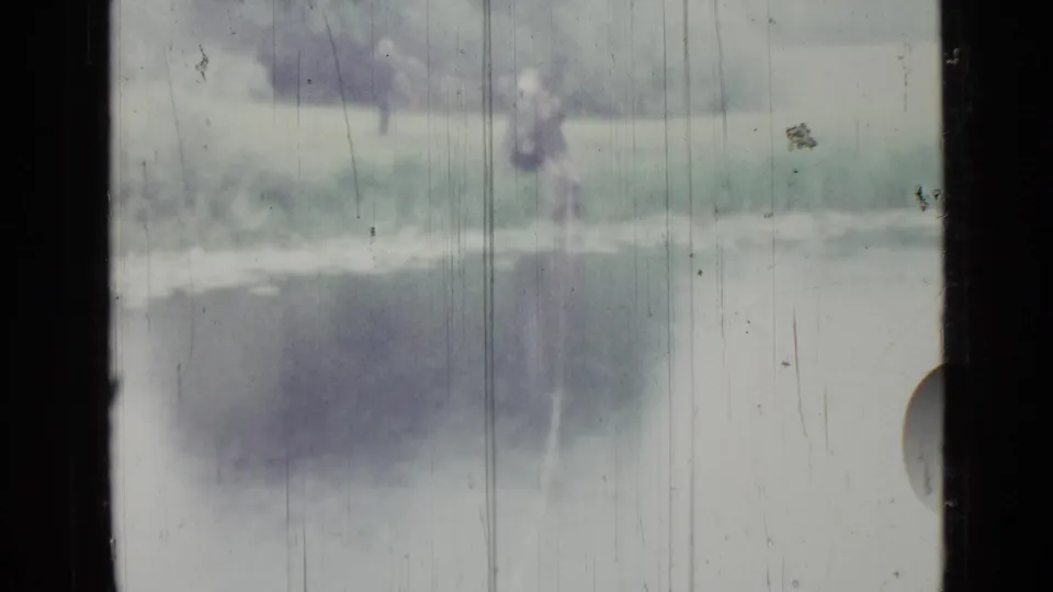 1967 Saint Petersburg 8mm frame with a distant person near the lakeshore and trees behind the bank.
