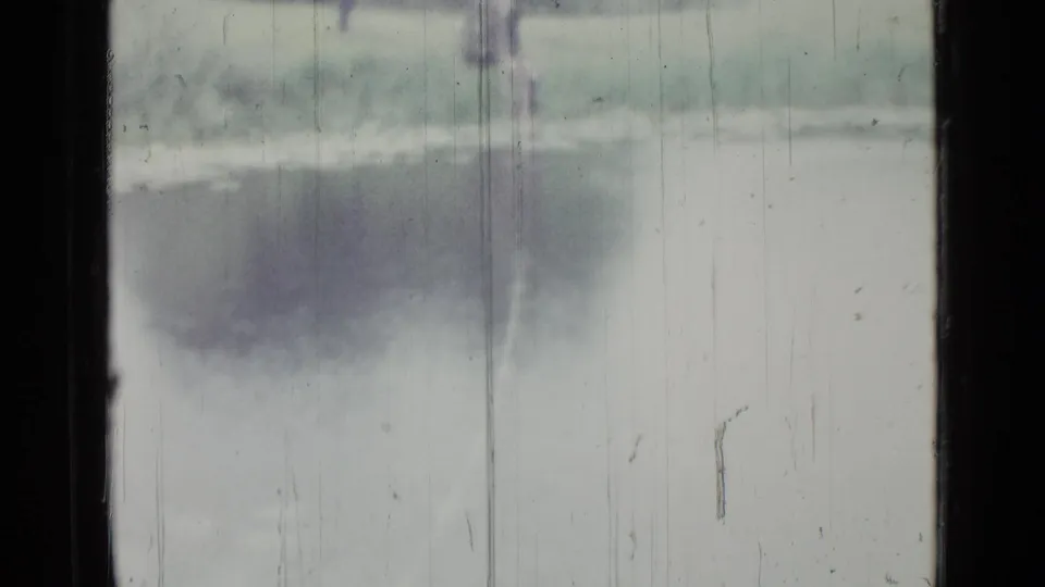 Soft 8mm frame from the 1967 Saint Petersburg lake scene, showing water, shoreline grass, and heavy film aging.