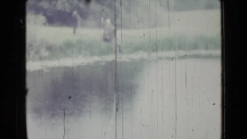 1967 Saint Petersburg 8mm frame showing two indistinct people by a small lake, with grass and trees behind them.