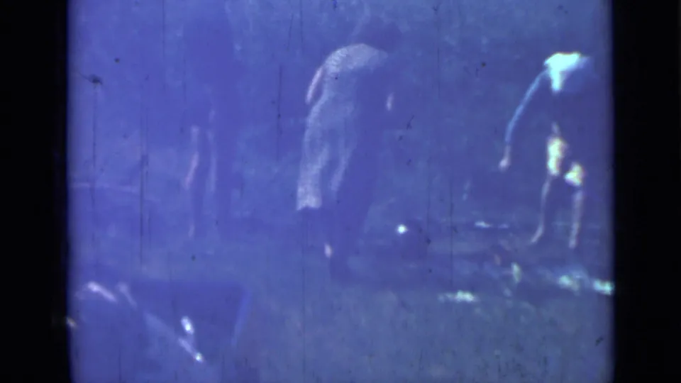 Women in a 1967 Saint Petersburg-area home movie bend near pans or food supplies in a rural outdoor camp setting.