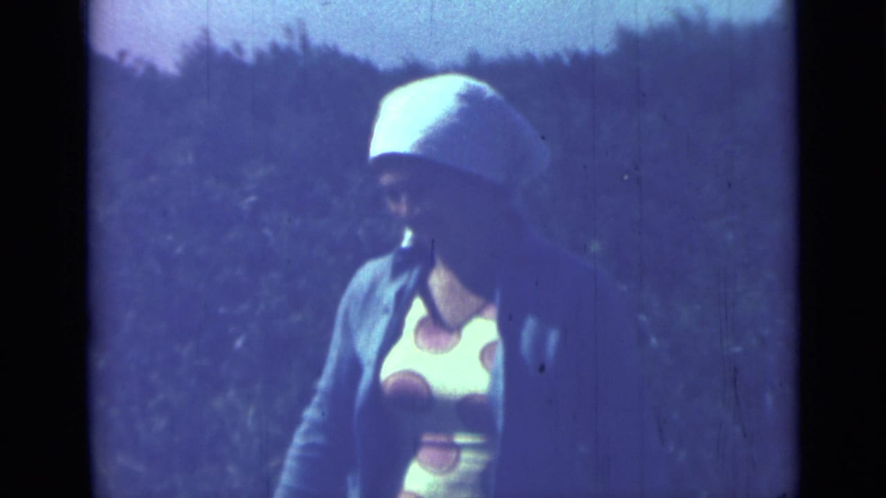 Woman in a polka dot dress and white head covering standing outdoors.