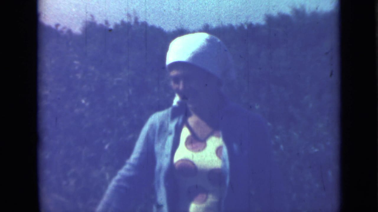 The same woman looks toward the camera outdoors, with cool blue 8mm color and a wooded background.