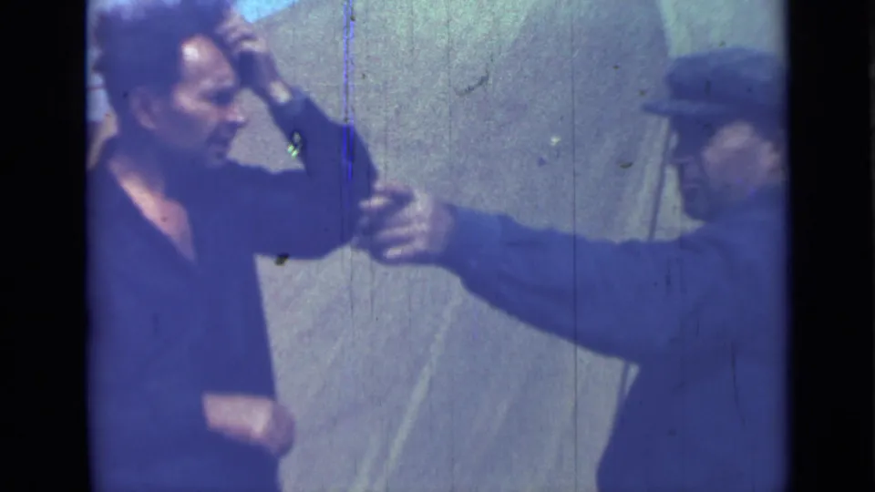 1967 Saint Petersburg 8mm frame showing two adult men outdoors, with one man in a cap extending an arm toward a man in a dark shirt.