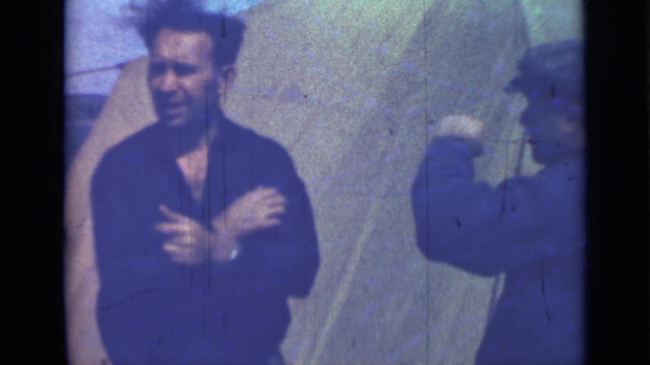 Man in a dark shirt faces camera while another capped man stands at the side with an arm raised.
