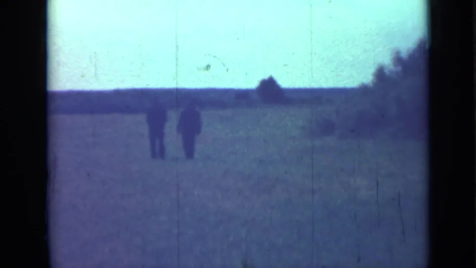 1967 Saint Petersburg 8mm frame with two small figures walking away across open ground toward a low horizon and tree line.