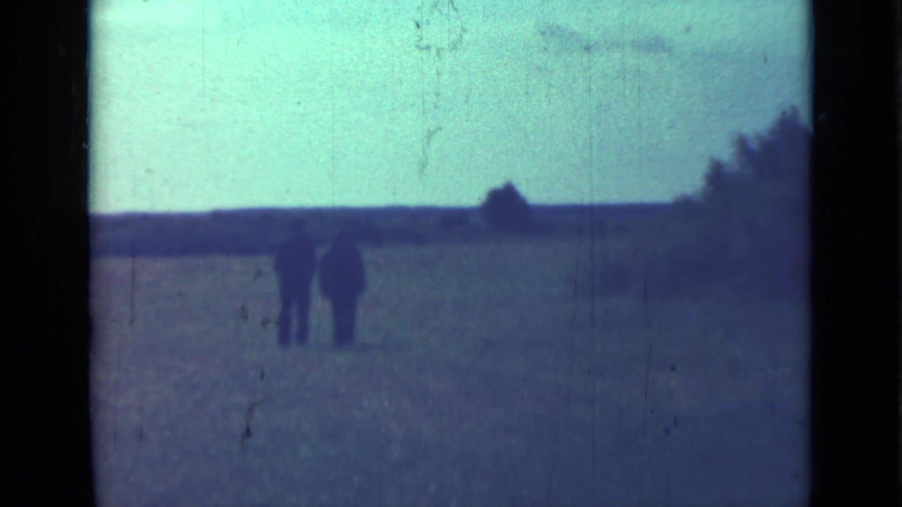 Two adult men in dark clothing walk side by side across a field in this 1967 Saint Petersburg home-movie frame.
