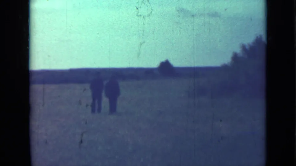 Two adult men in dark clothing walk side by side across a field in this 1967 Saint Petersburg home-movie frame.