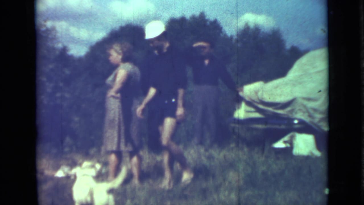 Adults at a 1967 outdoor gathering near Saint Petersburg stand by a small white dog and a car covered with light canvas.