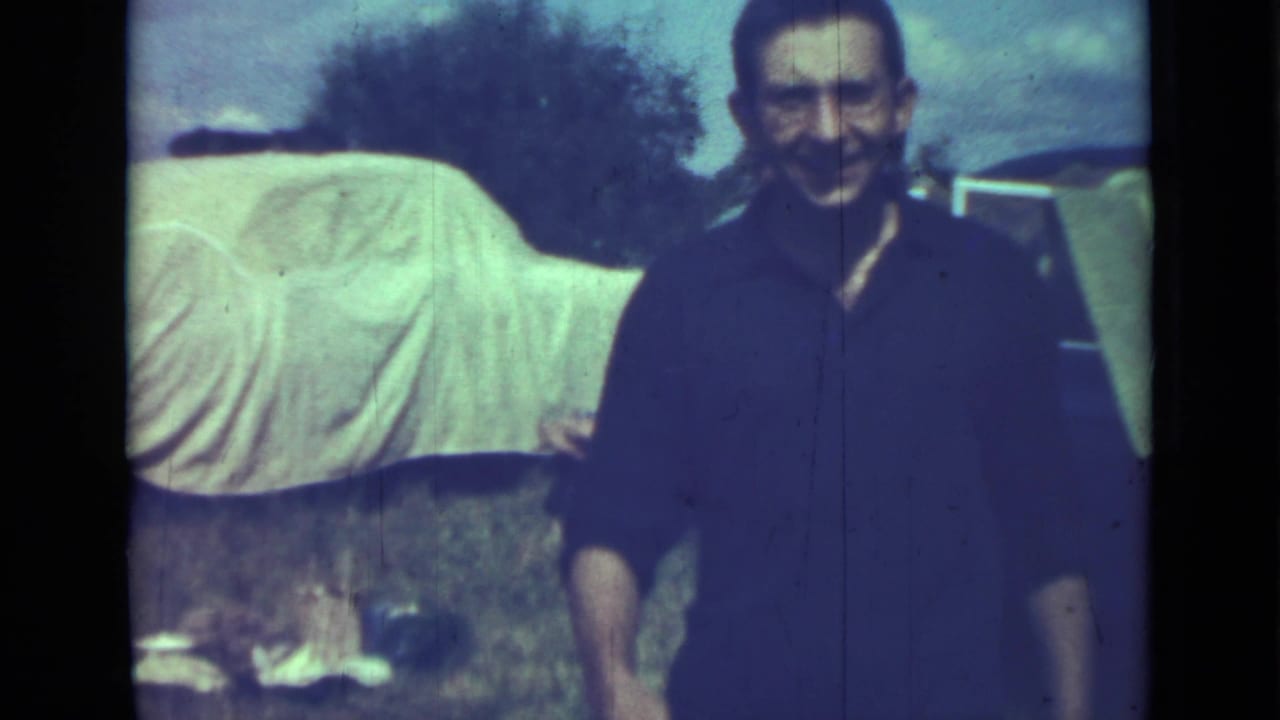 Man in a dark shirt stands near a white-covered car on grass.