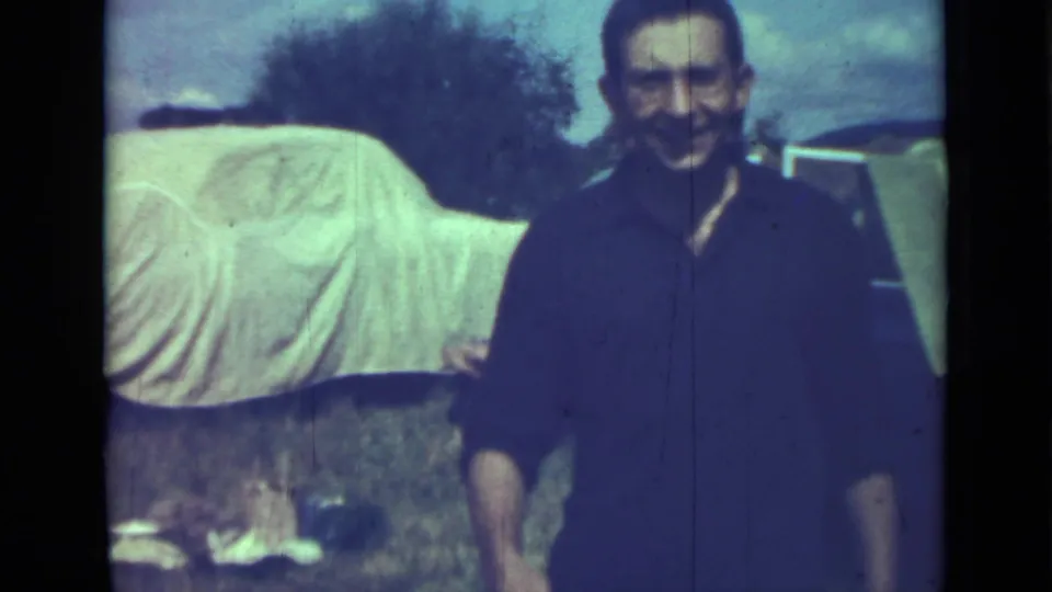 In supplied 1967 Saint Petersburg home-movie footage, a smiling man stands outdoors near a white-covered car on grass.