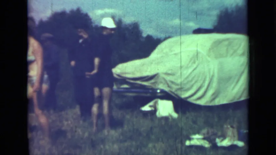 Adults gather near a white-covered car on grass in this supplied 1967 Saint Petersburg home-movie frame.