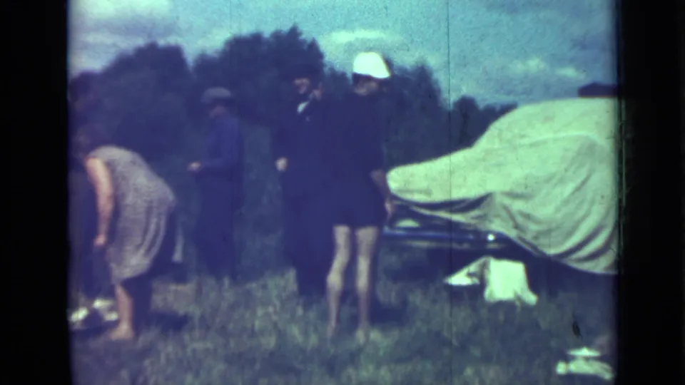 A small group stands around a tarp-covered car outdoors in the supplied 1967 Saint Petersburg home-movie footage.
