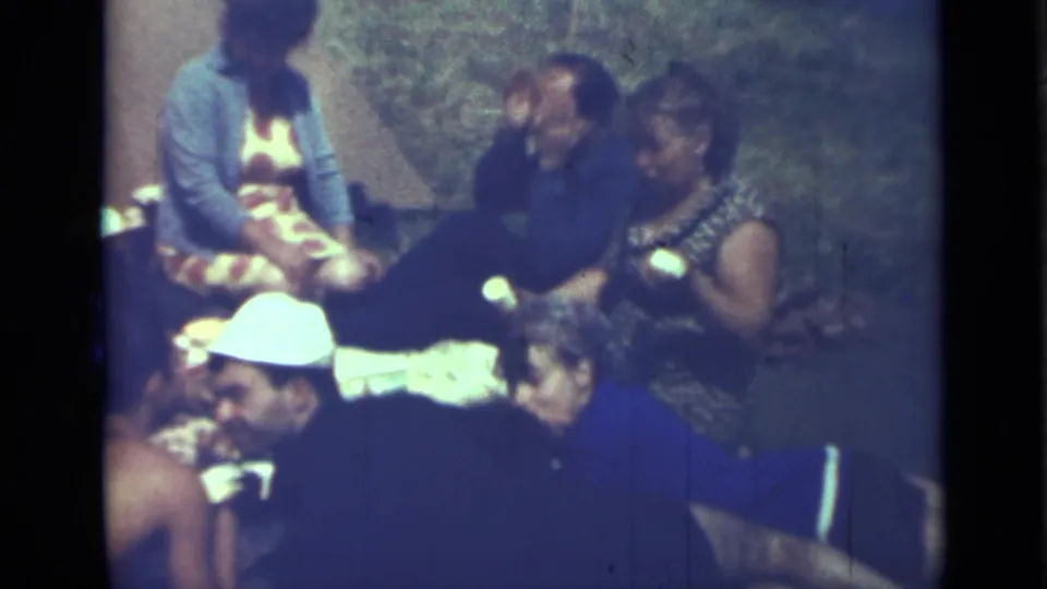 1967 8mm frame showing adults seated closely on the ground during an informal summer picnic in Saint Petersburg.