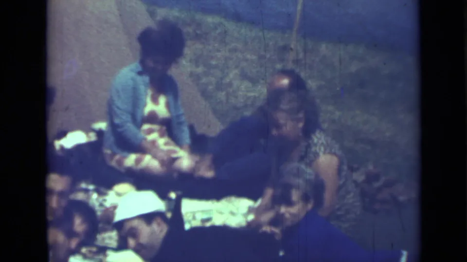 1967 Saint Petersburg 8mm frame of adults seated outdoors on the ground with picnic food and plates nearby.