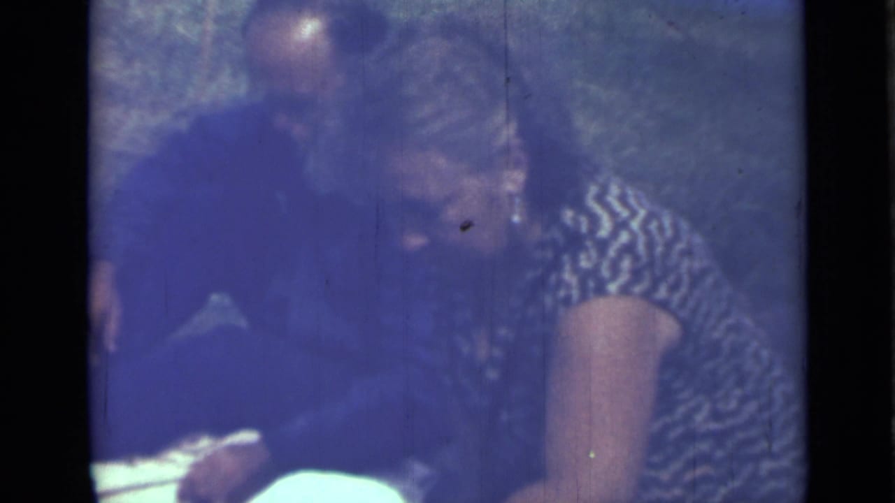 Adults seated close together on grass, partially obscured by dark film edges.