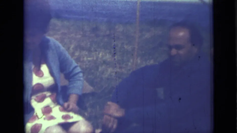 1967 Saint Petersburg home-movie still of two adults seated on grass, softened by the blue cast and grain of 8mm film.