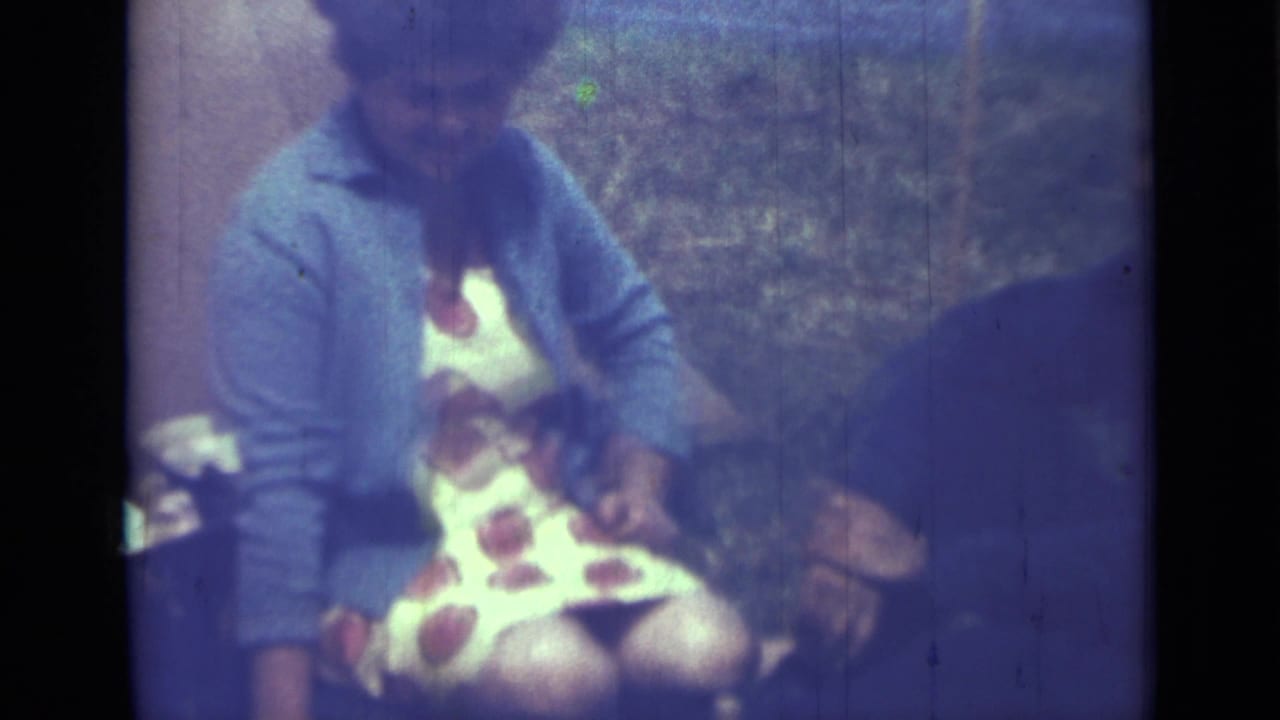 Seated person in a blue cardigan and polka-dot dress beside another figure.
