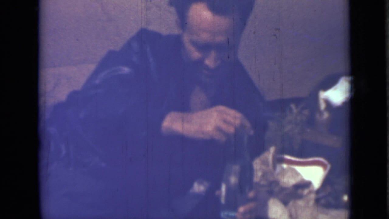 Man in a dark jacket handles a bottle at a dim indoor gathering.