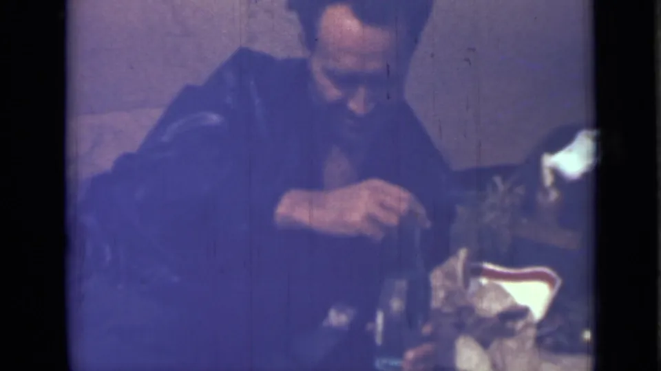 1967 Saint Petersburg 8mm frame showing a seated man in a dark jacket handling a bottle during an indoor gathering.