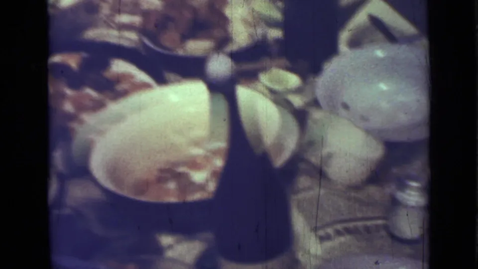 1967 Saint Petersburg home-movie frame with bowls, plates, food, a salt shaker, and a dark bottle crowded on a picnic table.
