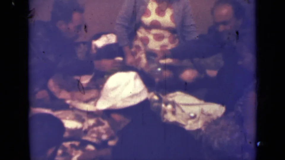 1967 Saint Petersburg home-movie frame showing a close indoor dining scene with adults seated around a crowded table.