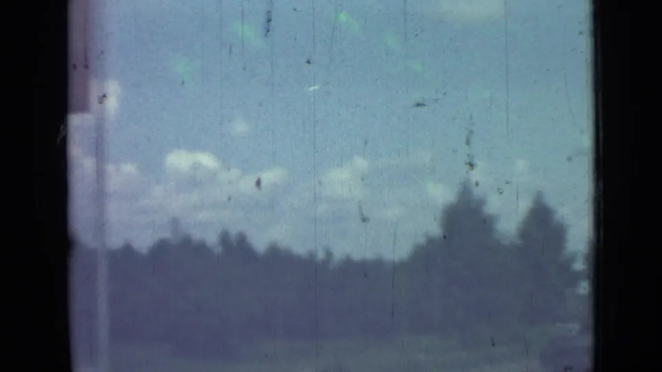 1967 8mm view from a moving vehicle near Saint Petersburg, showing a blurred roadside, trees, sky, and dark film borders.