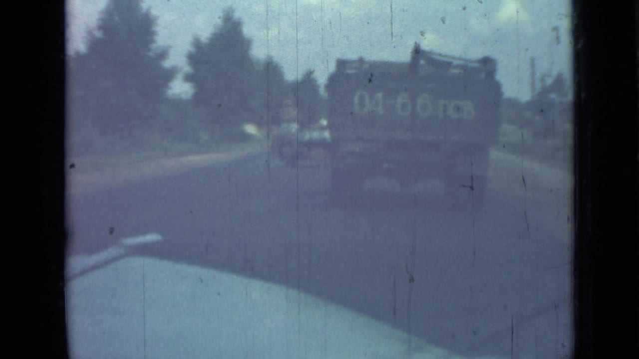 Truck ahead on a road seen past the edge of a car hood or windshield.