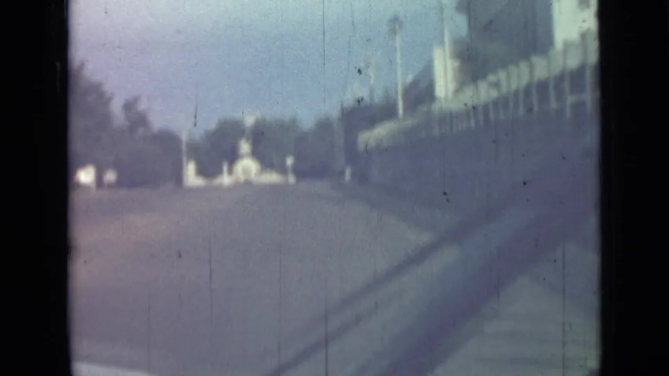 A moving-car view in 1967 Saint Petersburg shows a roadway, distant traffic or structures, and a roadside wall or building at right.
