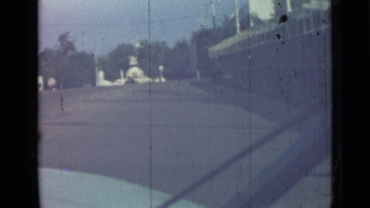 Blue-tinted street view with a distant white monument, trees, and a building edge at right.