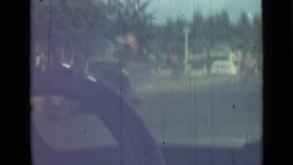 1967 Saint Petersburg street footage from a moving vehicle, with indistinct pedestrians, trees, and cars near the curb.