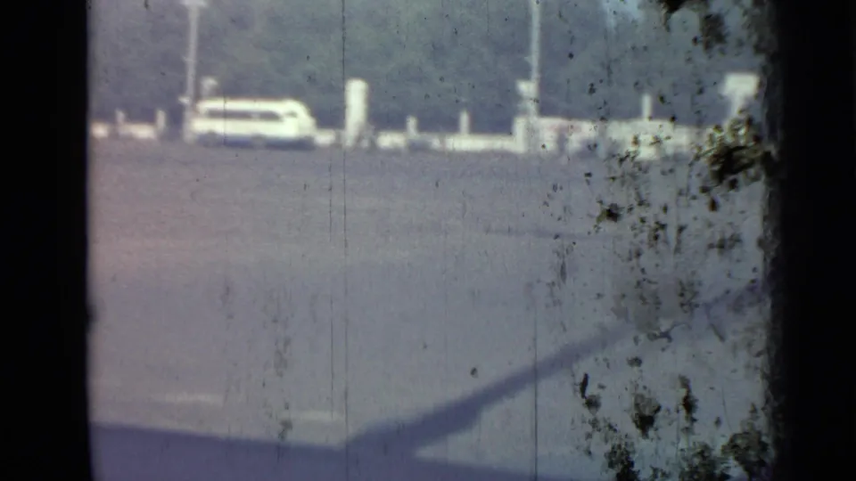 Soft 8mm frame of a parked car and white roadside posts across a sunlit paved lot in the Saint Petersburg clip.