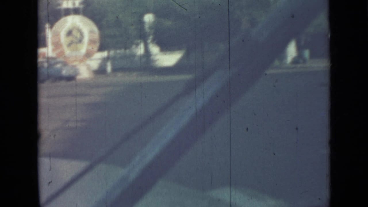 Soft 8mm frame of a road edge, poles, building facade, and circular structure in the distance.