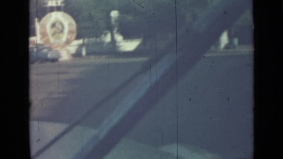 1967 Saint Petersburg home-movie frame showing a hazy roadside view with poles, a large building, and a distant circular feature.